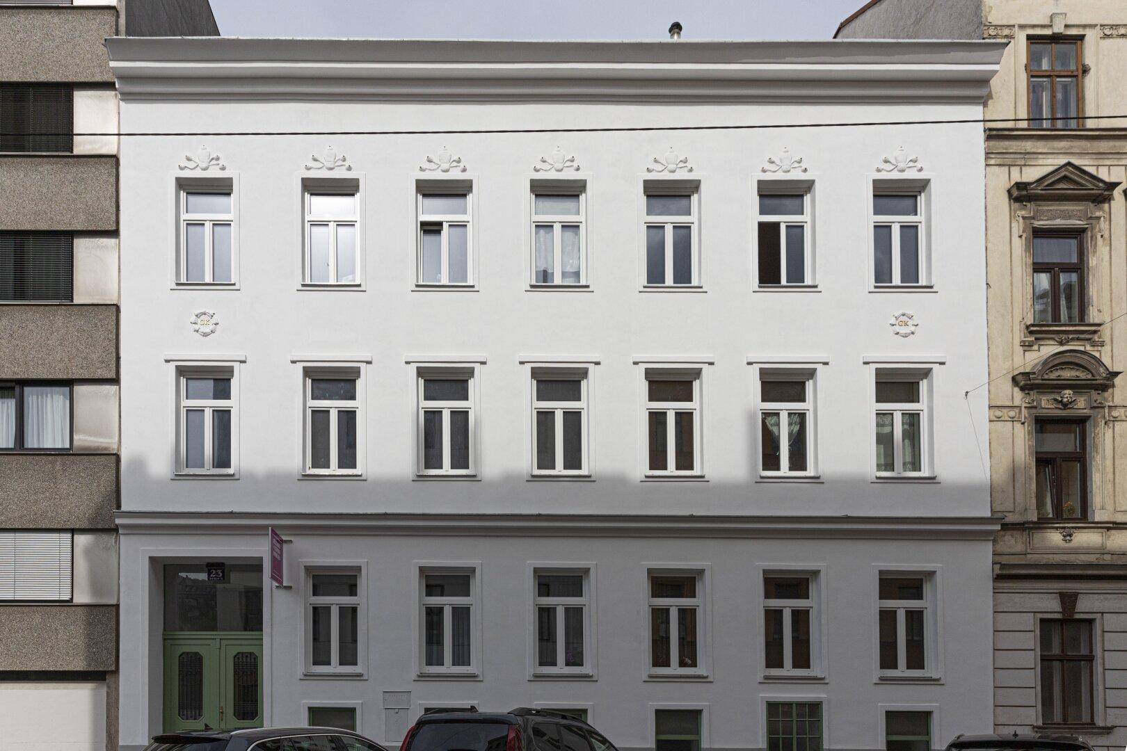 Frontale Ansicht der frisch renovierten weißen Fassade eines Wohngebäudes bei Tageslicht.