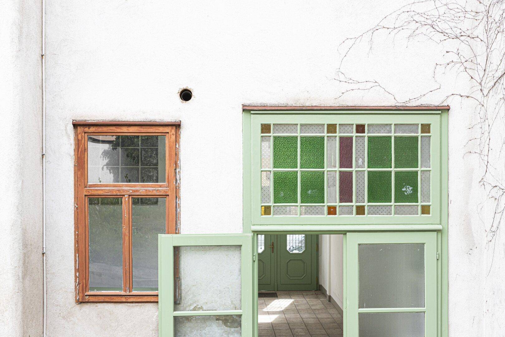 Detailansicht eines Fensters und einer Tür mit farbigem Bleiglas in einer alten Fassade.