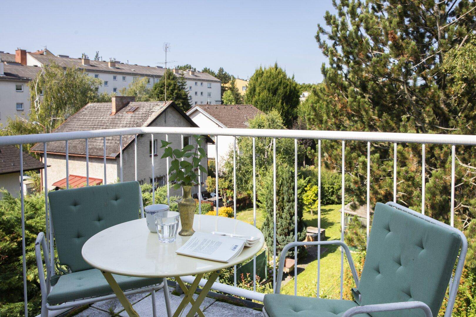 Möblierter Balkon mit Tisch und Stühlen, umgeben von Bäumen und Blick auf die Nachbarschaft.