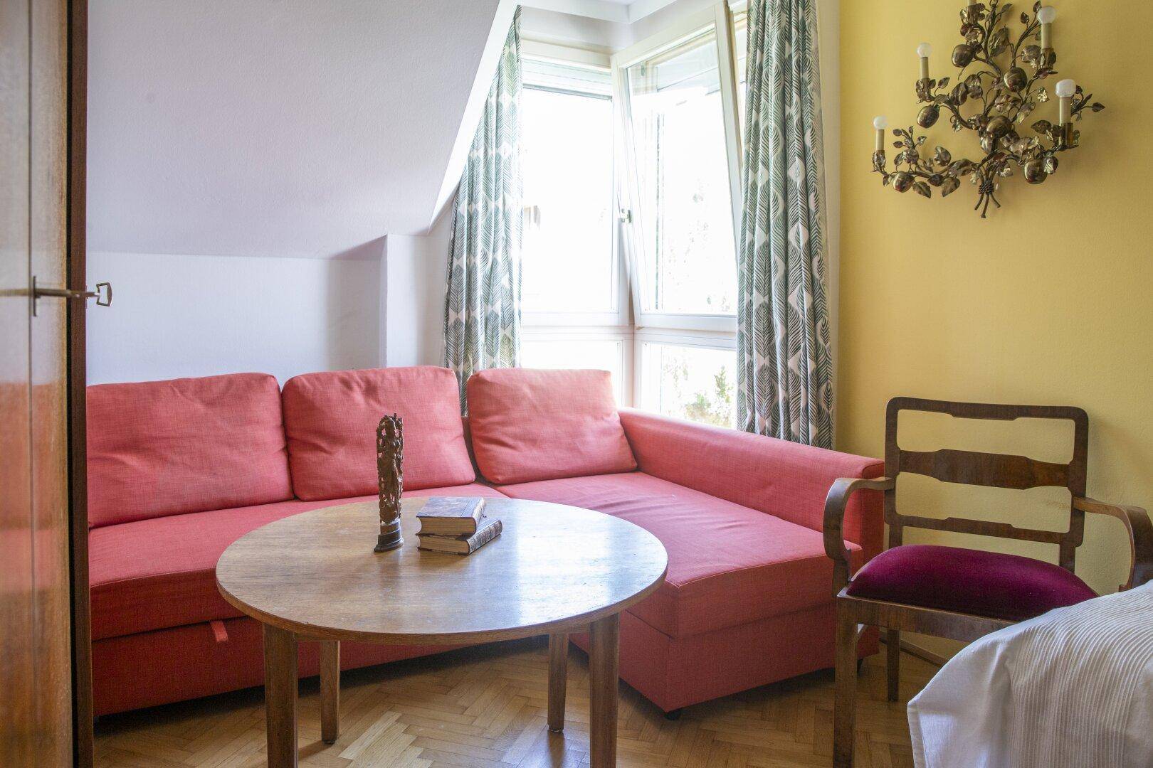 Gemütlicher Wohnbereich mit rotem Sofa, Couchtisch und großem Fenster, das viel Licht hereinlässt.