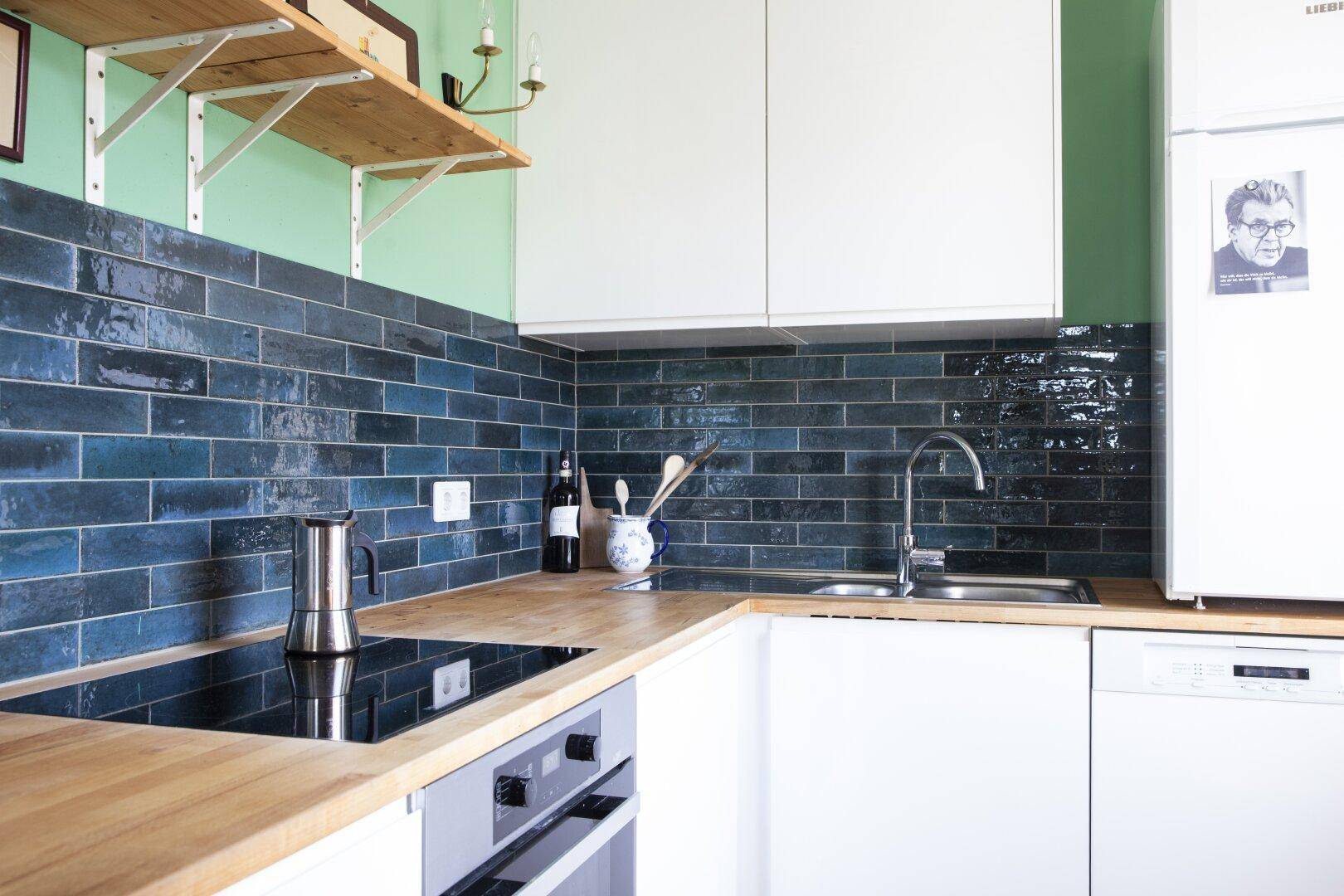 Moderne Küche mit weißen Schränken, Holz-Arbeitsplatte und blauen Fliesen als Spritzschutz.