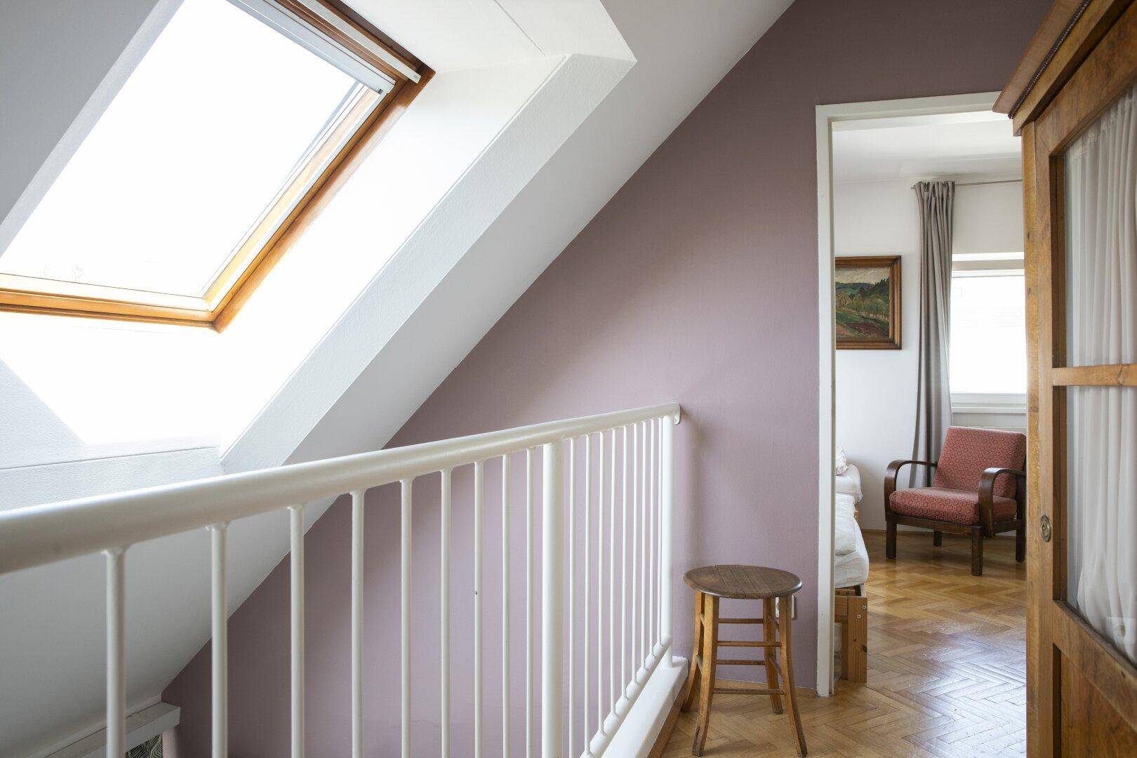 Heller Flur im Dachgeschoss mit Dachfenster, Geländer und Zugang zu einem weiteren Zimmer.