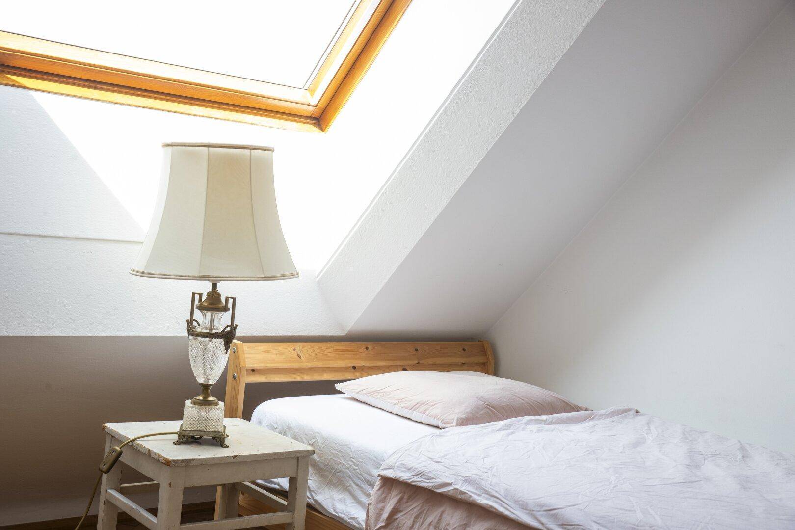 Schlafzimmer im Dachgeschoss mit Einzelbett und großem Dachfenster für viel Tageslicht.