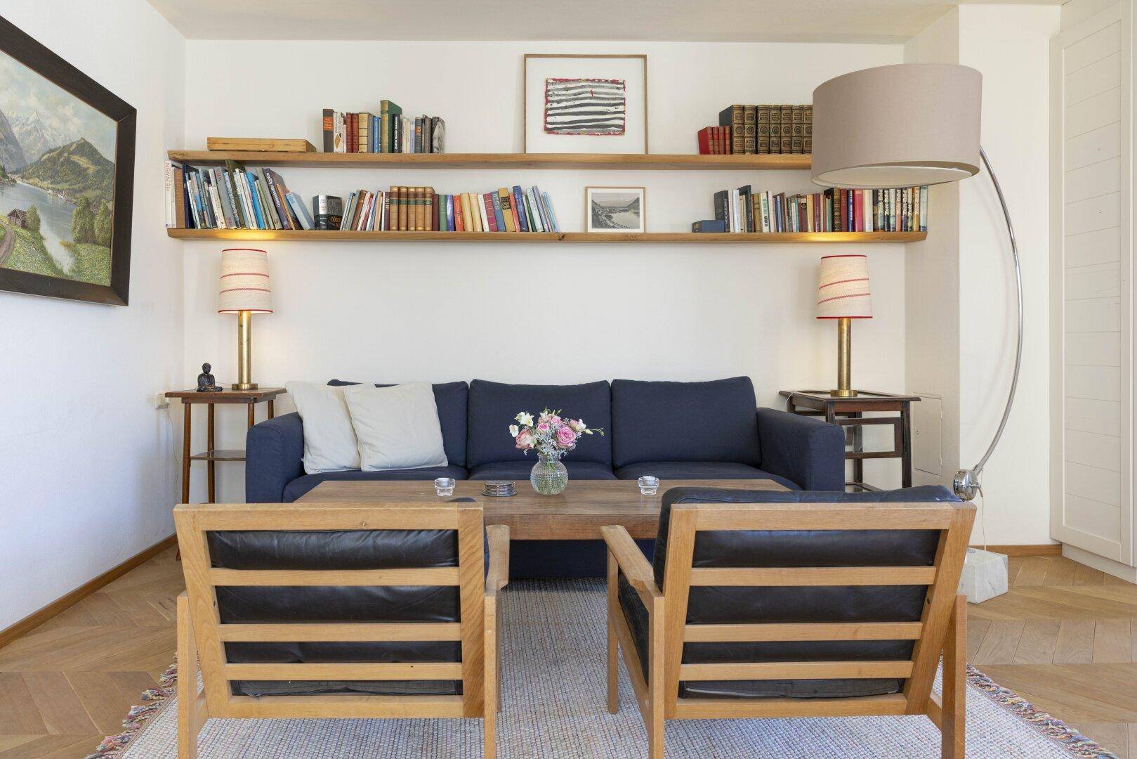 Gemütliches Wohnzimmer mit blauem Sofa, Holztisch und Bücherregalen an der Wand.