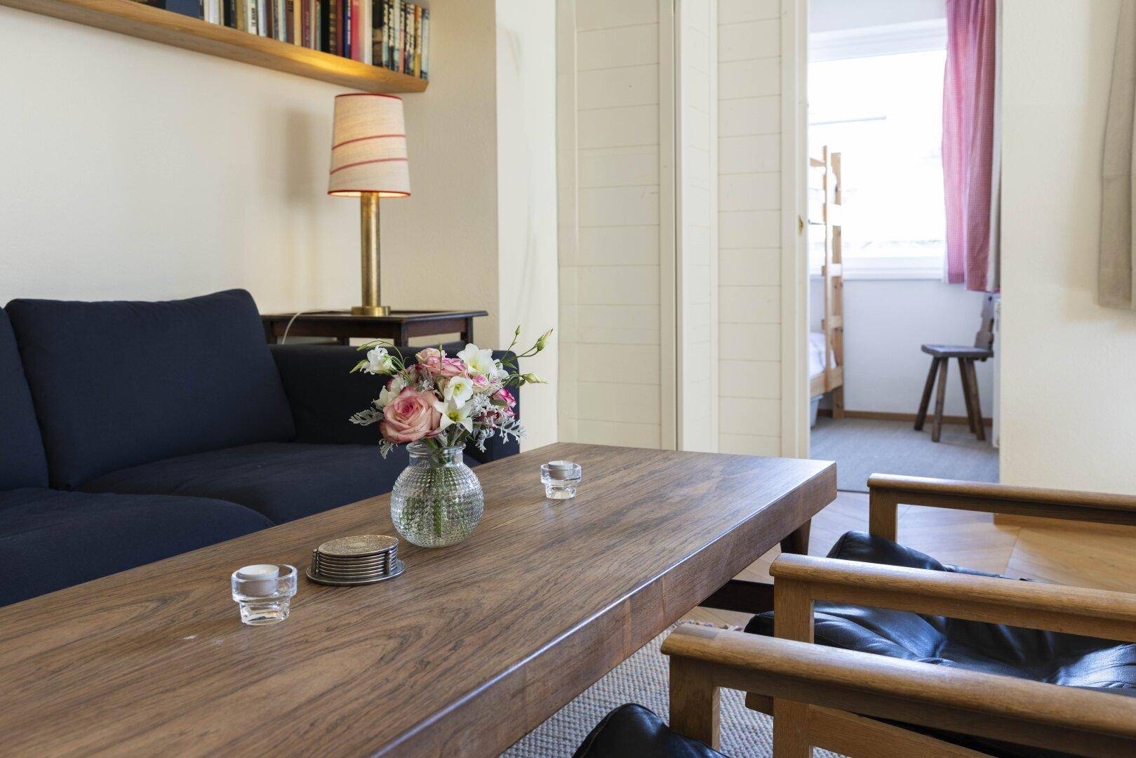 Nahaufnahme eines Holztisches mit Blumenstrauß im Wohnzimmer, angrenzend an einen Schlafbereich.