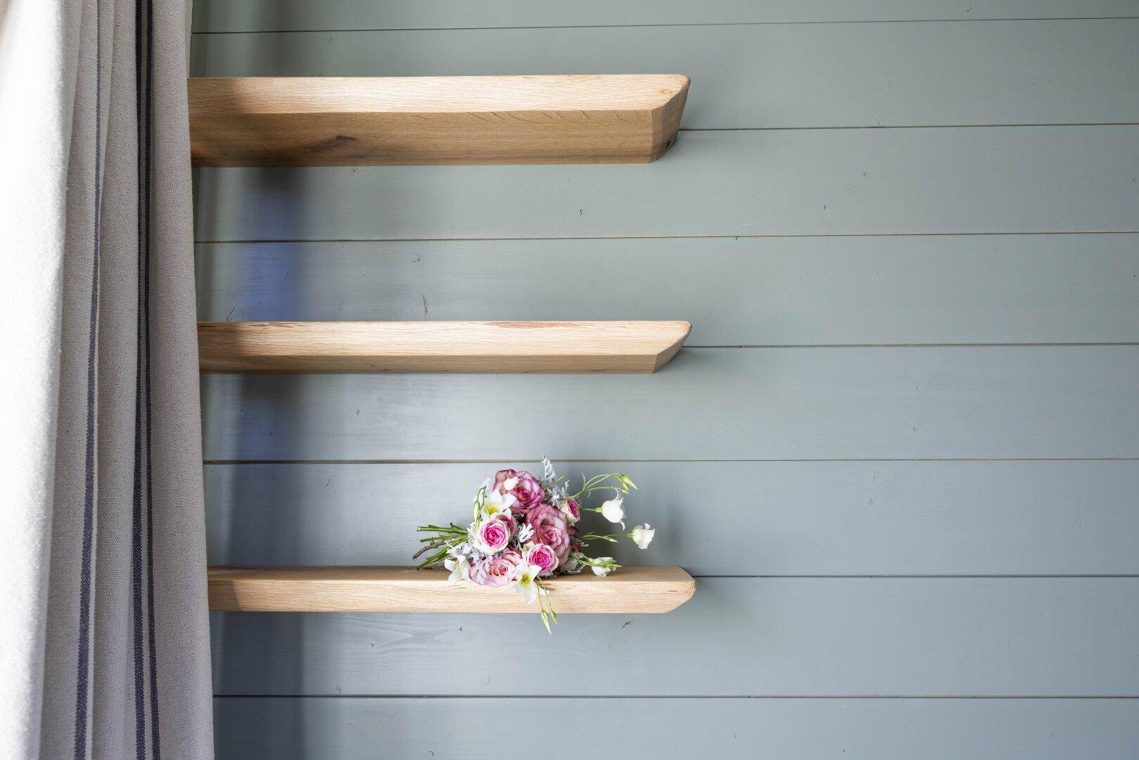 Detailansicht von Holzregalen an einer grünen Wand mit einem Blumenstrauß.