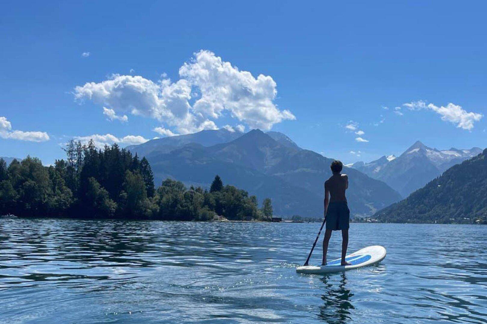 Person auf einem Stand-Up-Paddle-Board auf einem See mit Bergpanorama im Sommer.