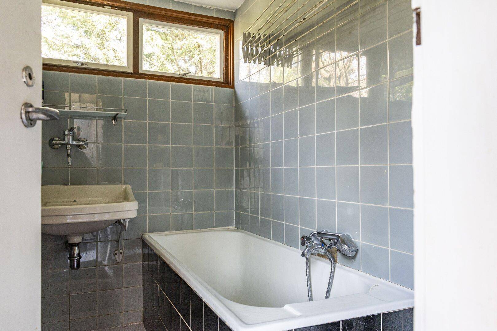 Badezimmer mit hellblauen Fliesen, Badewanne und Waschbecken, ausgestattet mit einem Fenster.