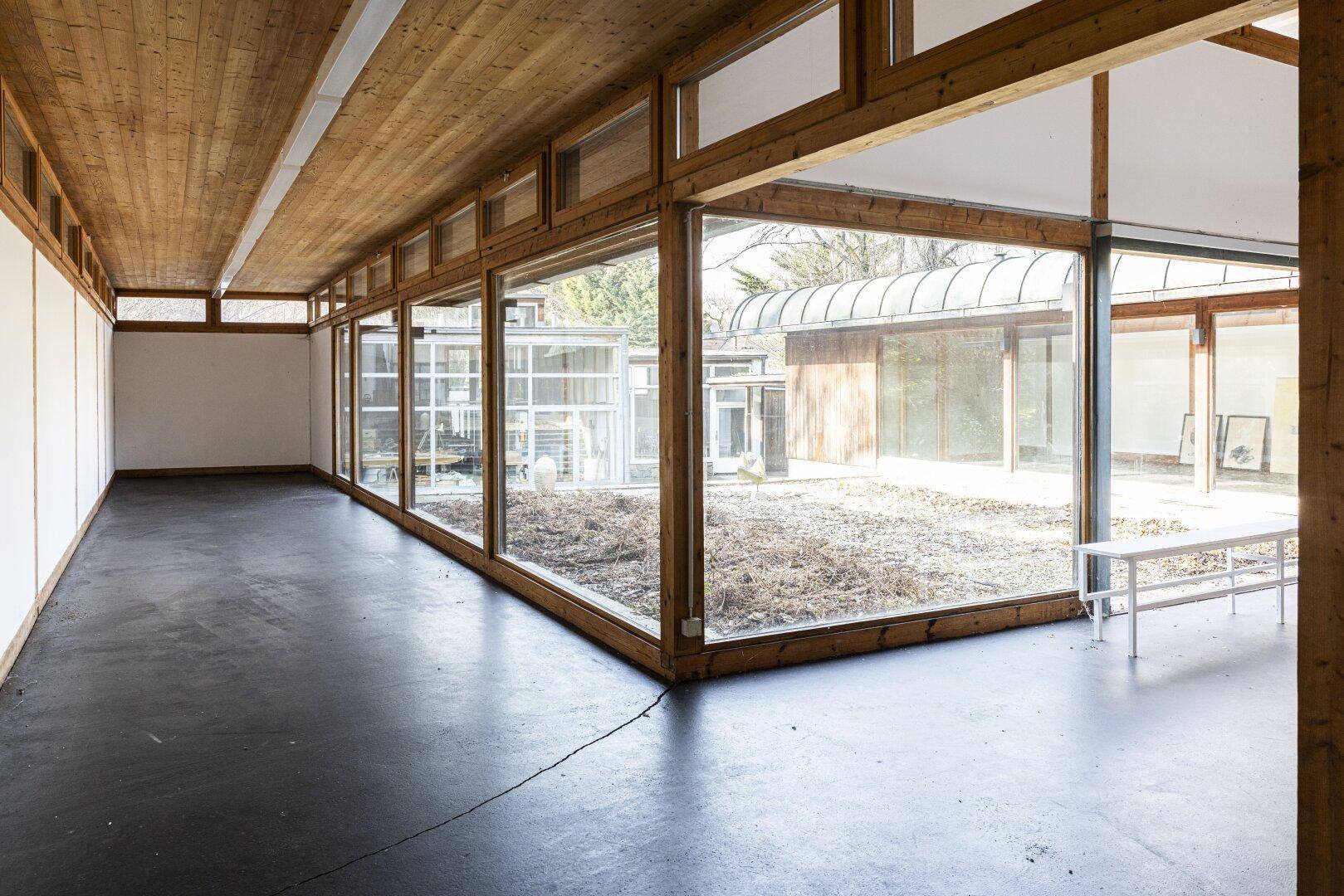 Geräumiger, heller Raum mit Holzdecke und großen Fenstern, die den Blick ins Grüne freigeben.