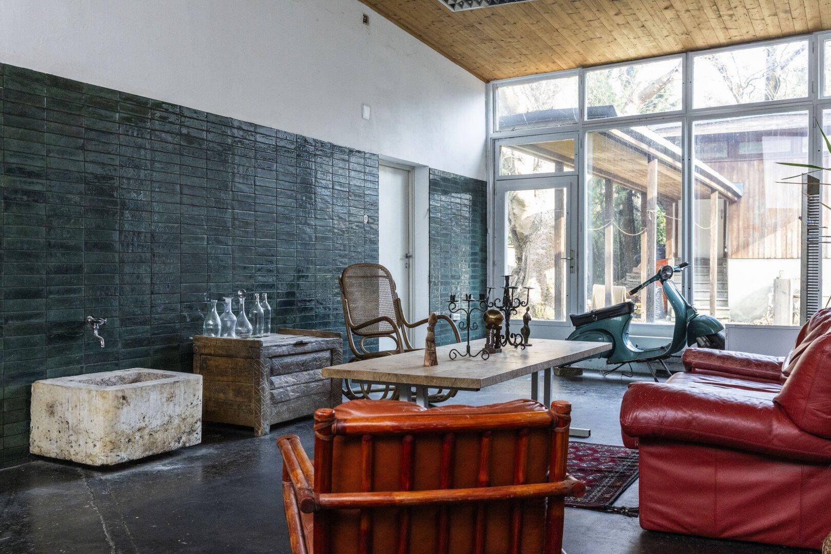 Wohnzimmer mit Ledersofas, Holztisch und großen Fenstern, die den Außenbereich zeigen.
