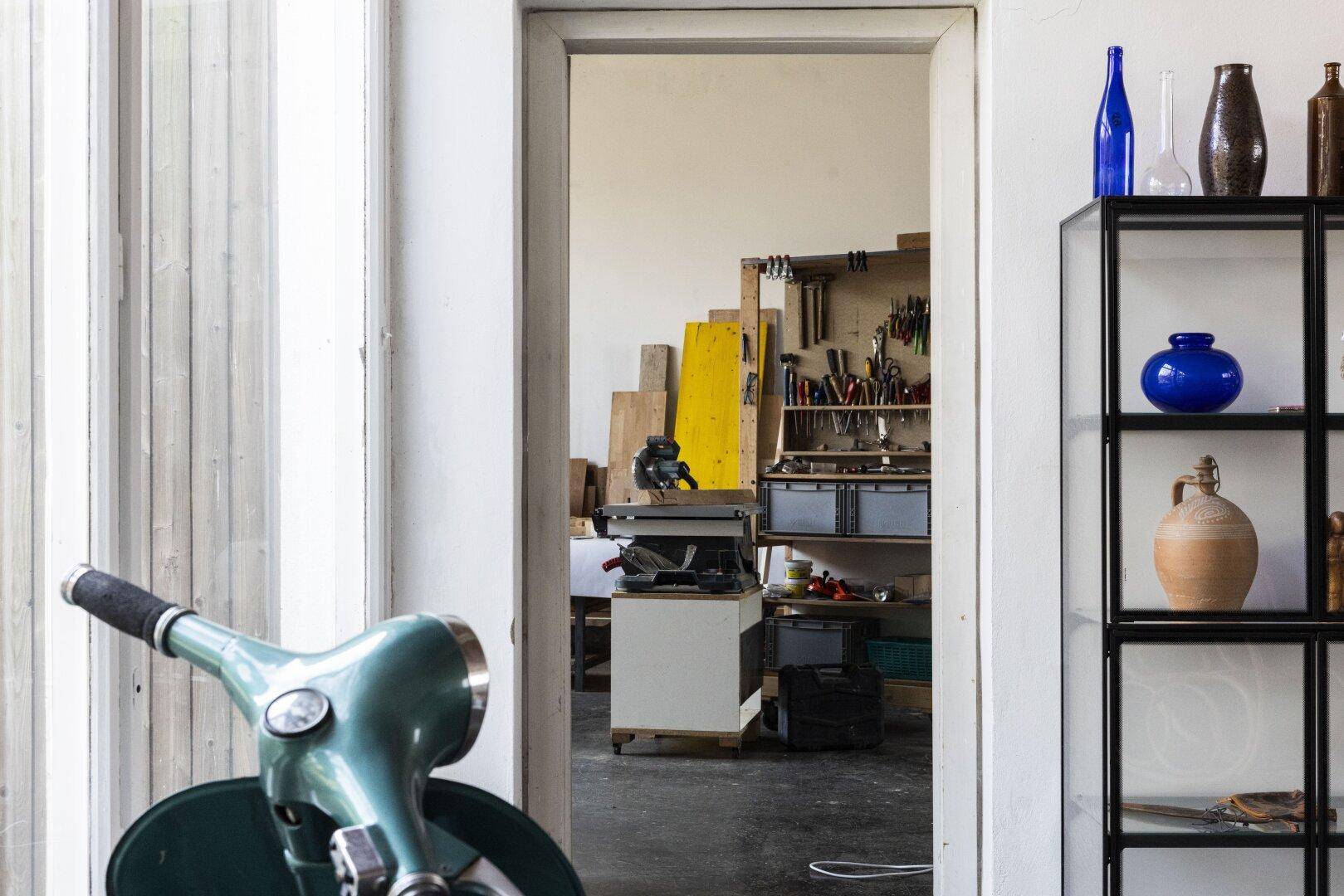 Blick in eine Werkstatt mit Werkzeugen und Holzmaterialien, gesehen durch eine offene Tür.