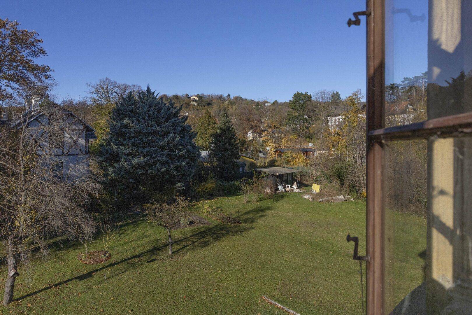 Weitläufiger Blick aus dem Fenster auf den großen Garten und die hügelige Landschaft.