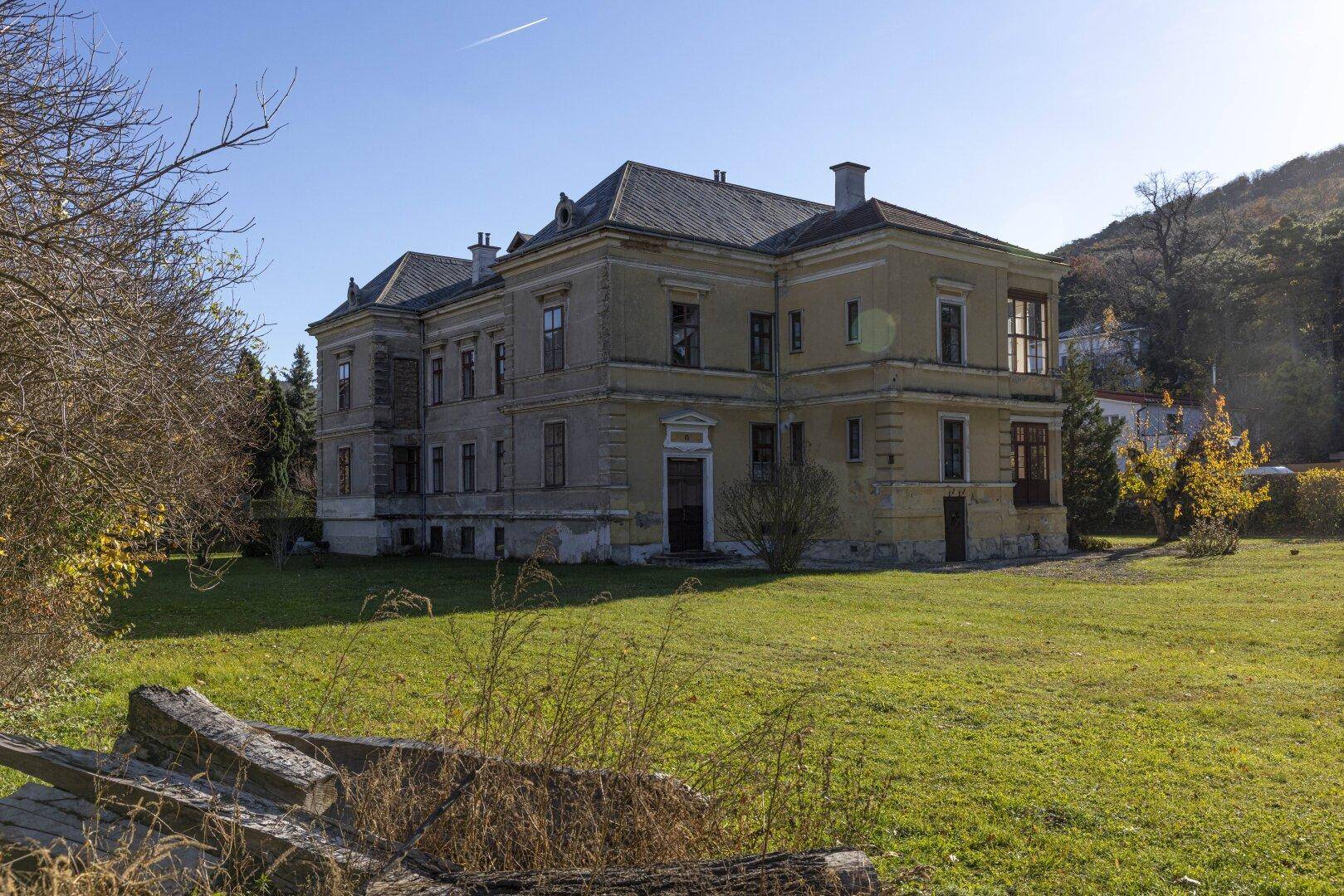 Historische Villa von der Seite mit großem Garten und Blick auf die umliegende Natur.