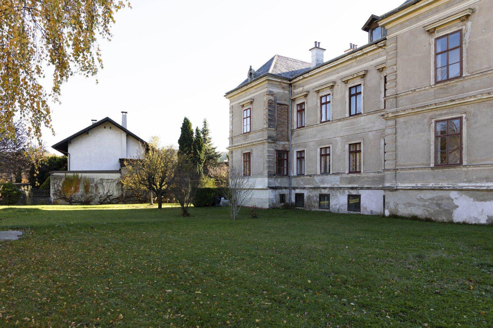 Historische Villa von der Seite mit weitläufigem Garten und angrenzendem Nebengebäude.