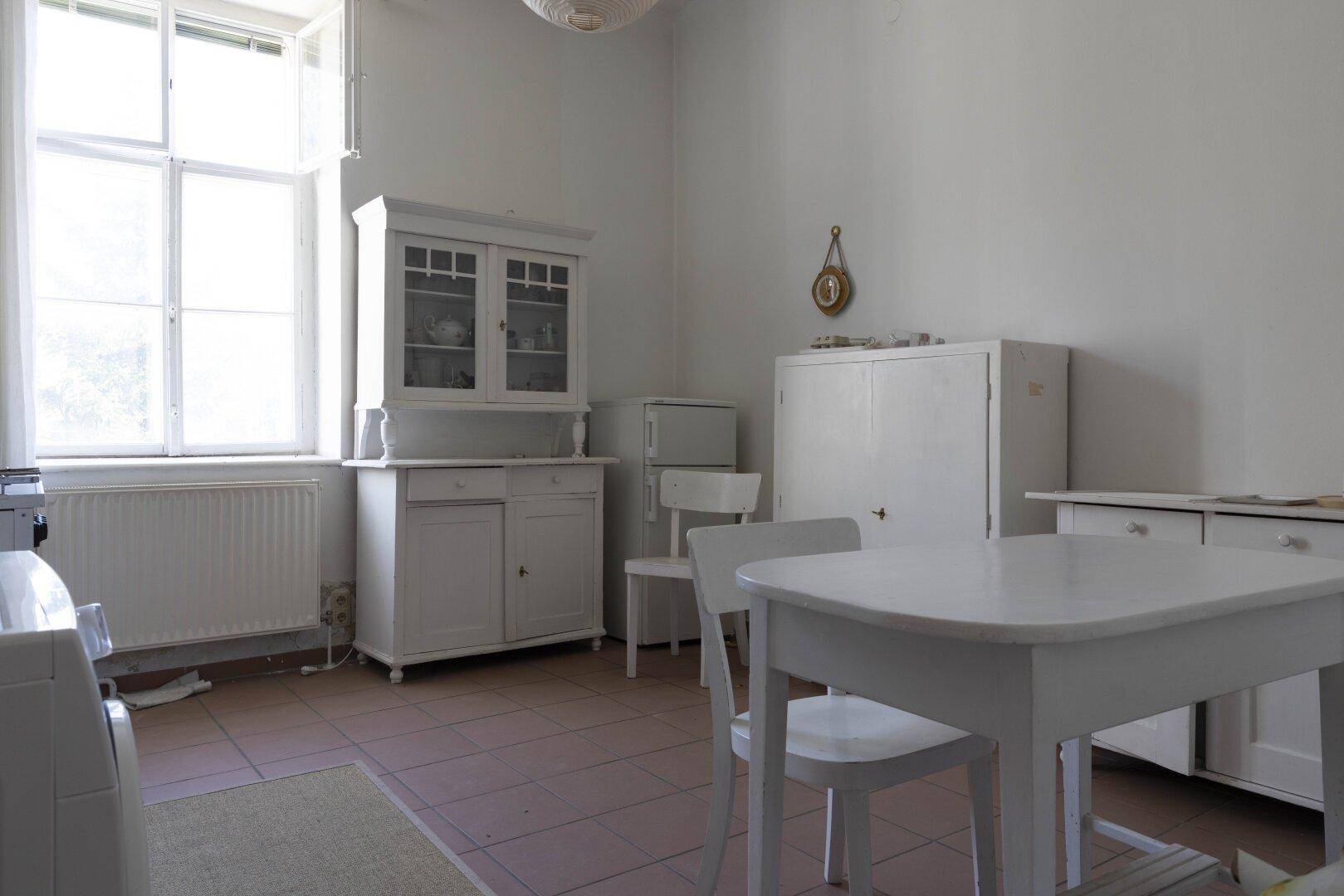 Helle Küche mit traditionellen weißen Schränken und Esstisch, bereit für eine Modernisierung.