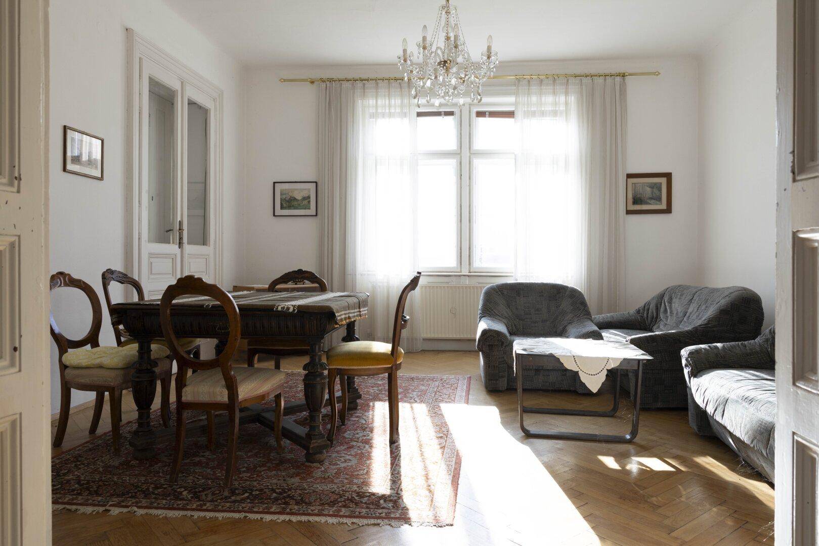 Eleganter Wohn-Essbereich mit Kronleuchter, Parkettboden und antiken Möbeln.