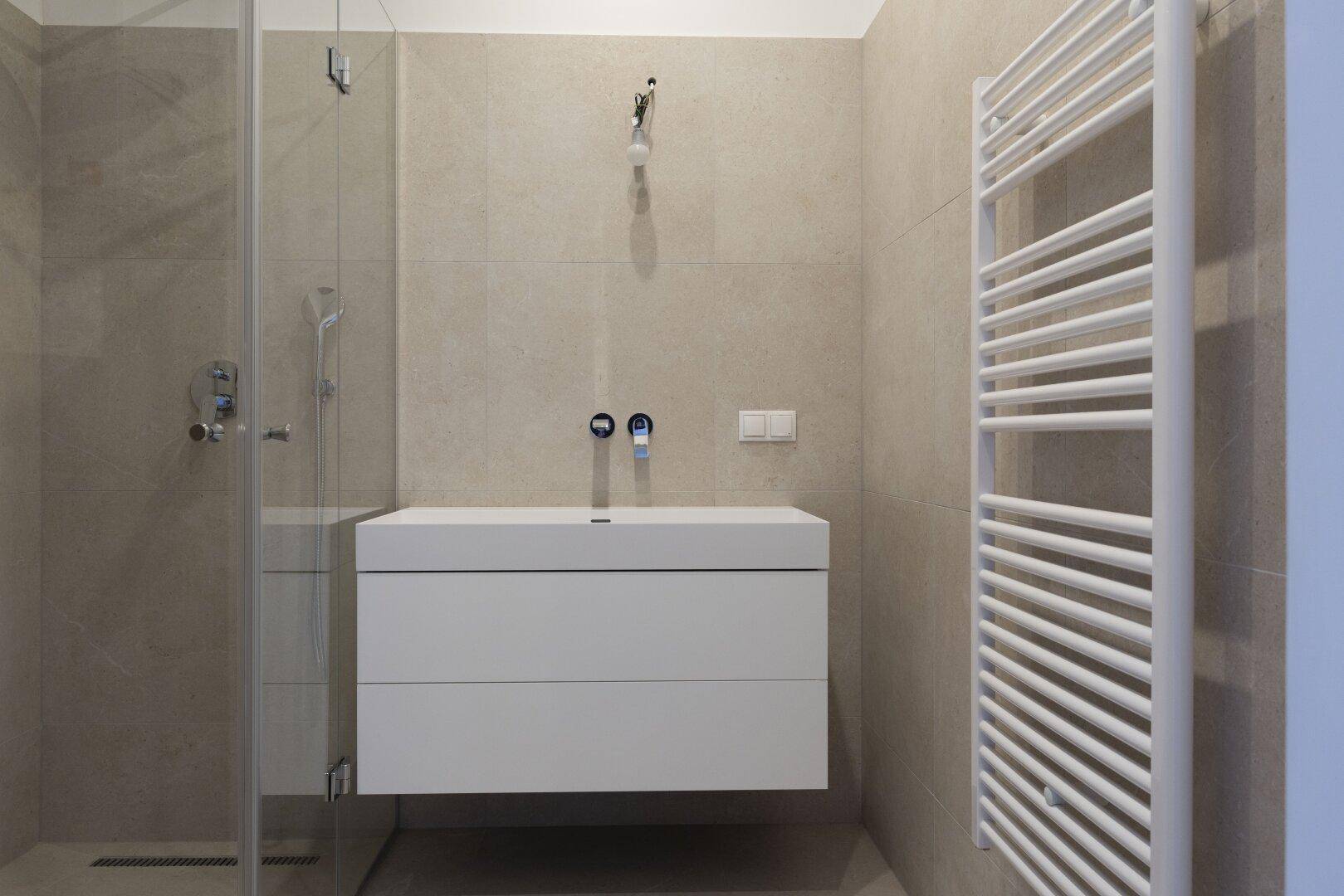 Modernes Badezimmer mit beigefarbenen Fliesen, schwebendem Waschtisch, begehbarer Dusche und Handtuchheizkörper.