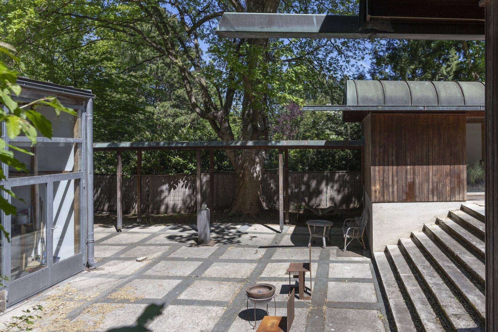 Außenbereich mit gepflasterter Terrasse und moderner Architektur, umgeben von Bäumen und Grün.