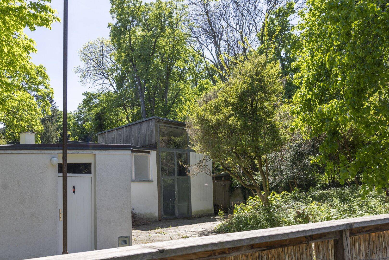 Nebengebäude mit weißer Fassade und umgebendem Grün, eingebettet in die Natur.