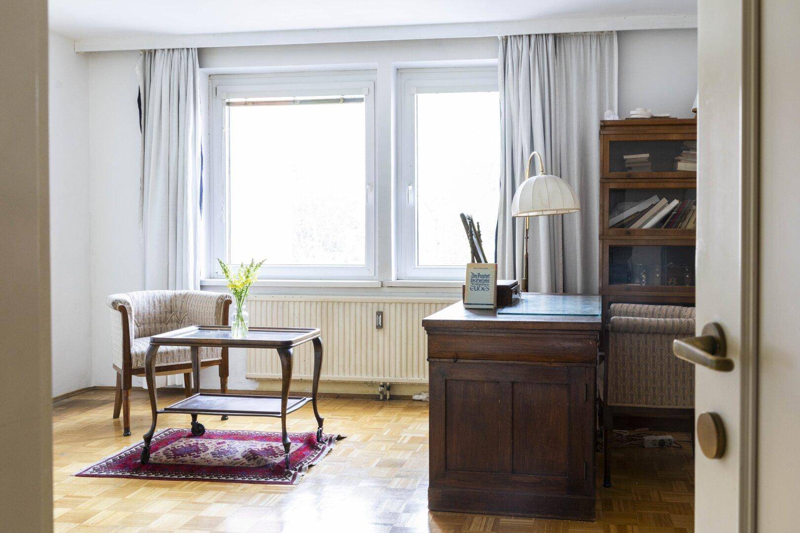Helles Arbeitszimmer mit Parkettboden, Schreibtisch und großem Fenster.