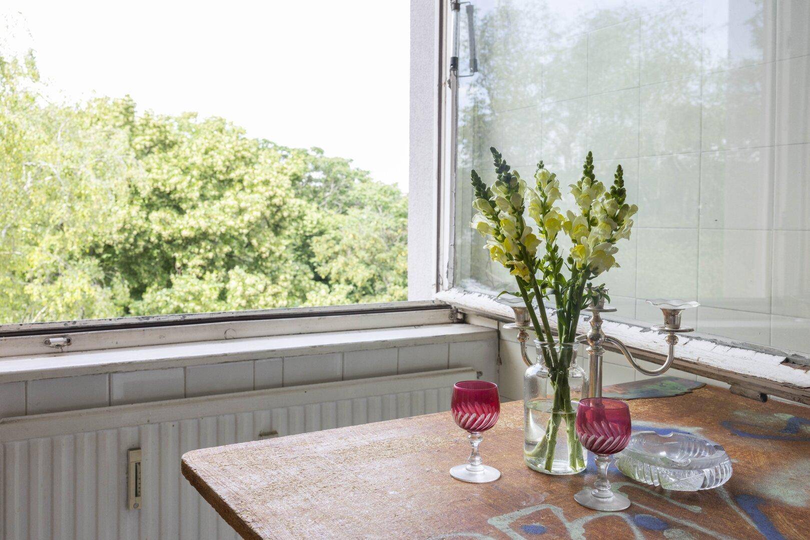 Fenster mit Blick ins Grüne, dekoriert mit Blumen und Weingläsern.
