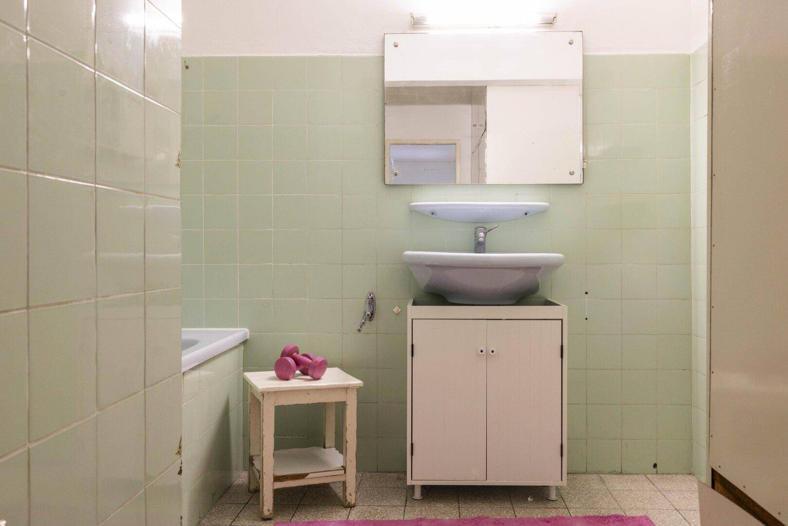 Badezimmer mit hellgrünen Fliesen, Waschbecken und Badewanne.