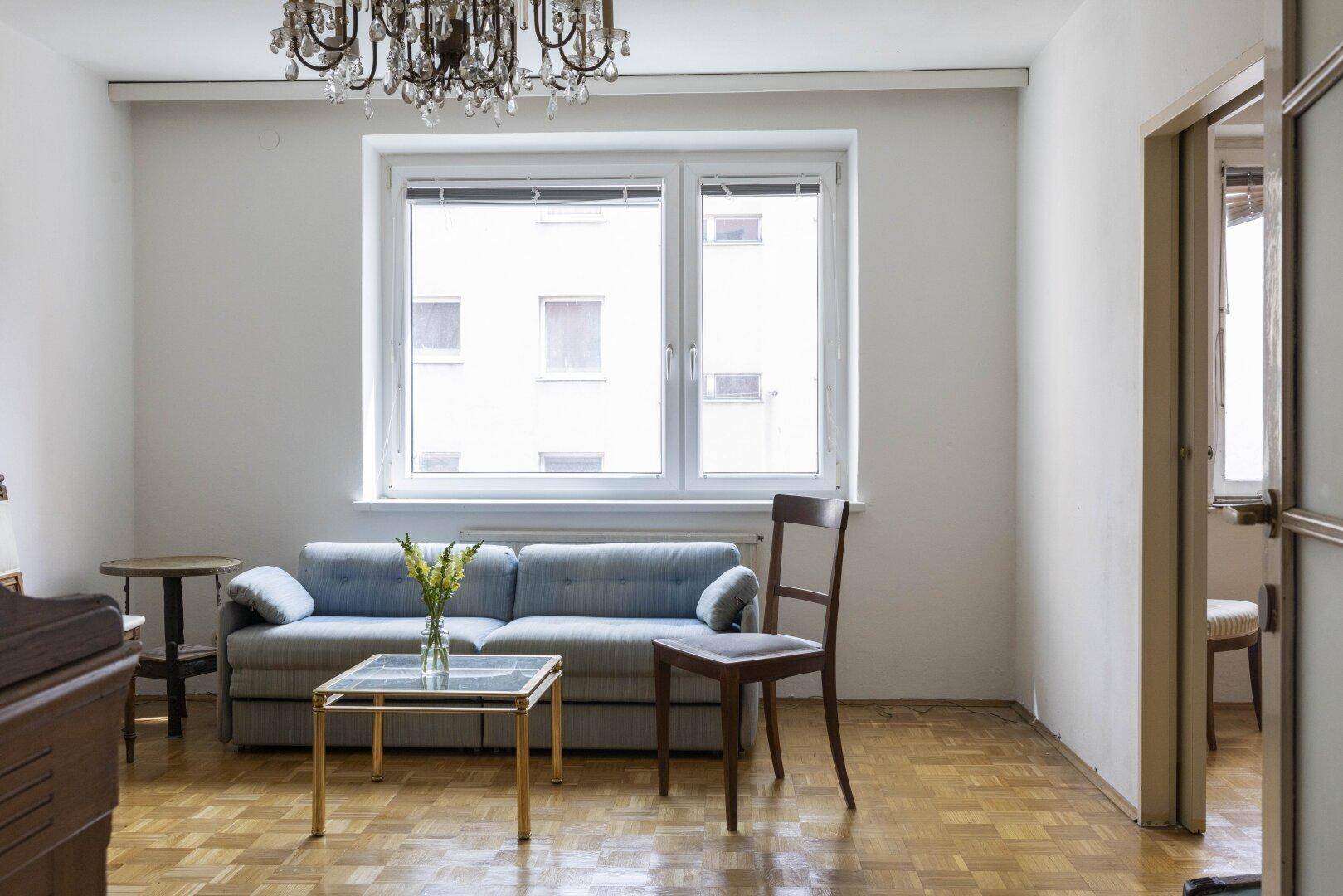 Wohnzimmer mit Parkettboden, Sofa, Kronleuchter und großem Fenster.