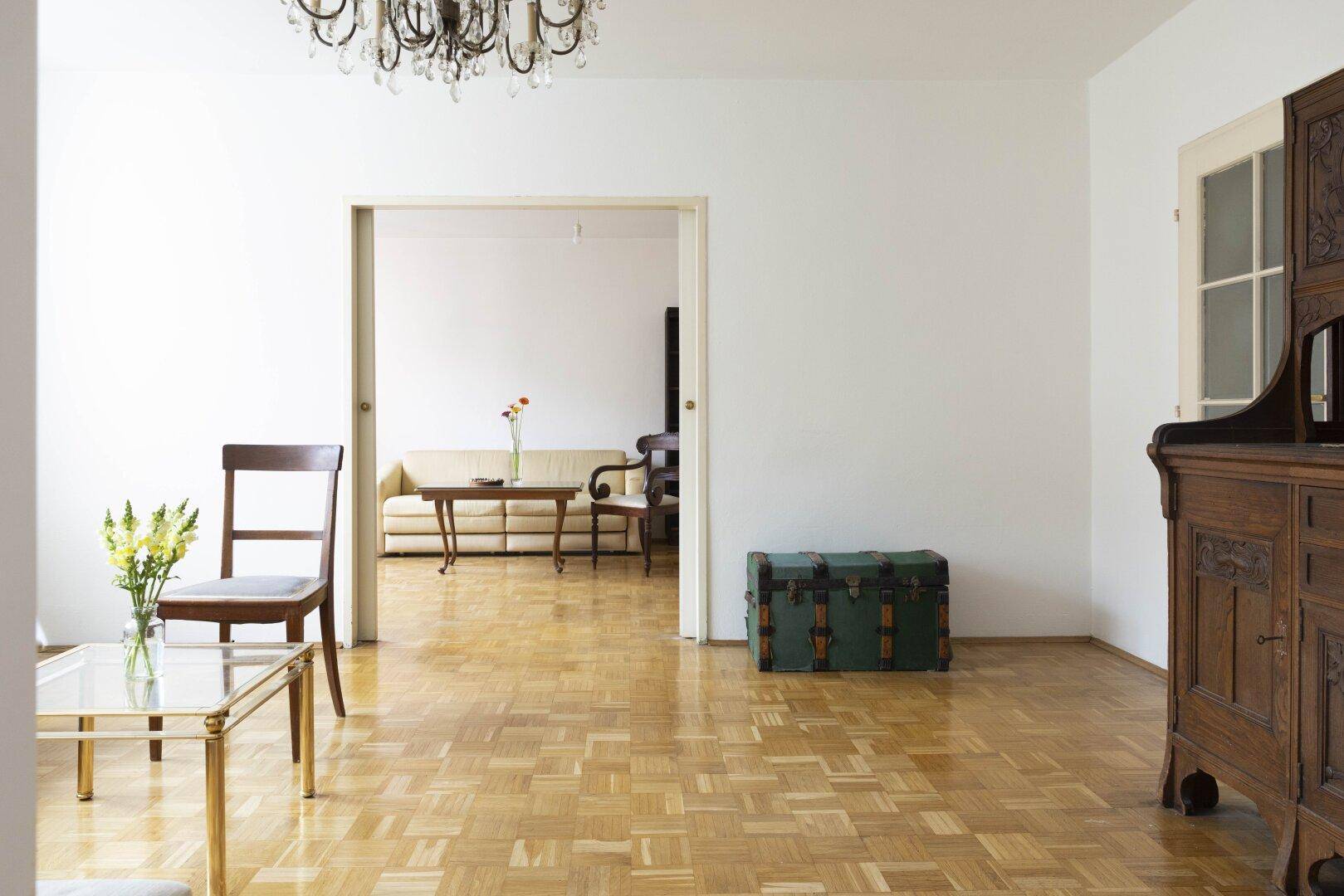 Geräumiger Wohnbereich mit Parkettboden und Durchgang zu einem weiteren Zimmer.