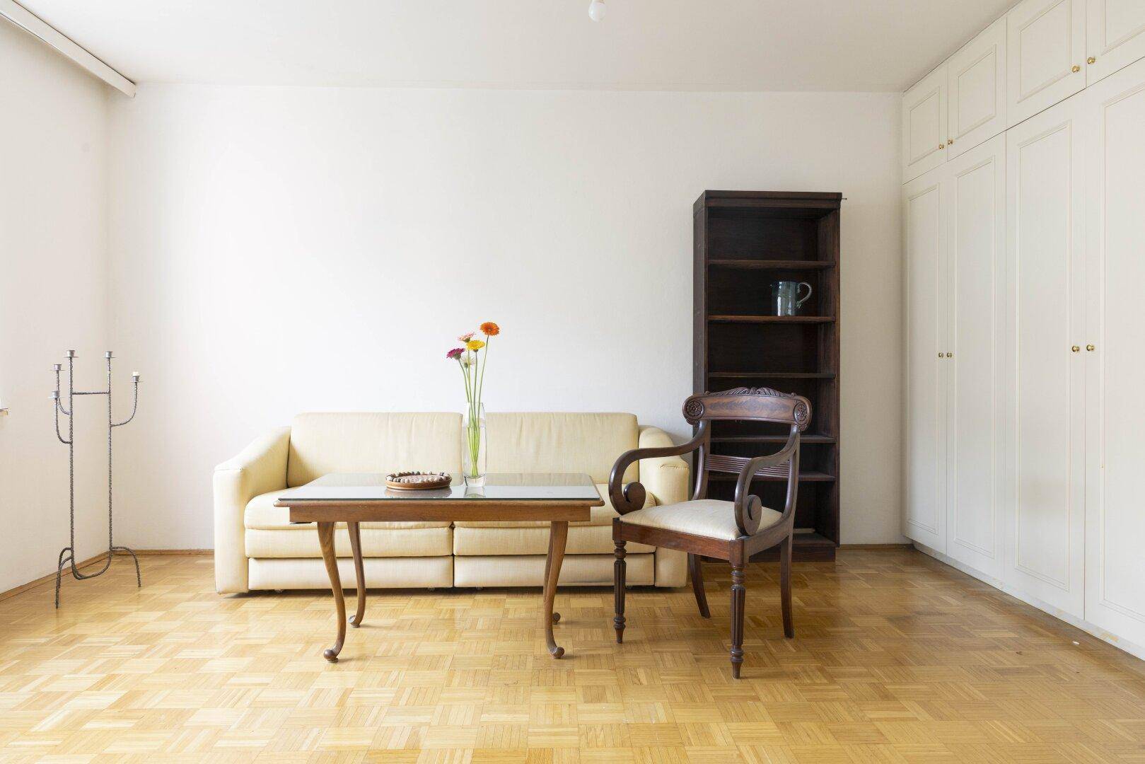 Helles Wohnzimmer mit Sofa, Bücherregal und integrierten Kleiderschränken.