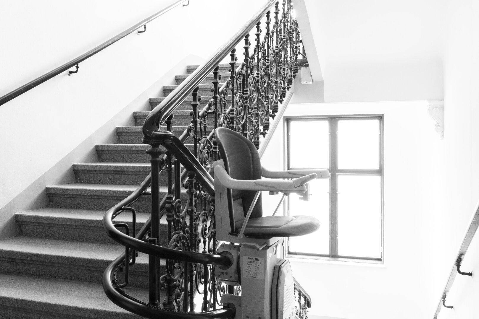 Historisches Treppenhaus mit schmiedeeisernem Geländer und einem Treppenlift für Barrierefreiheit.