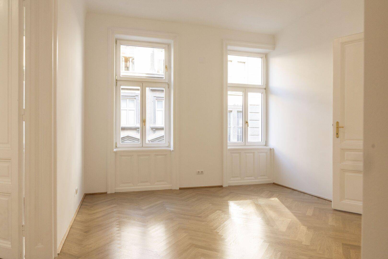 Helles Zimmer mit zwei großen Fenstern und Fischgrätparkett, ideal für Wohn- oder Schlafbereich.