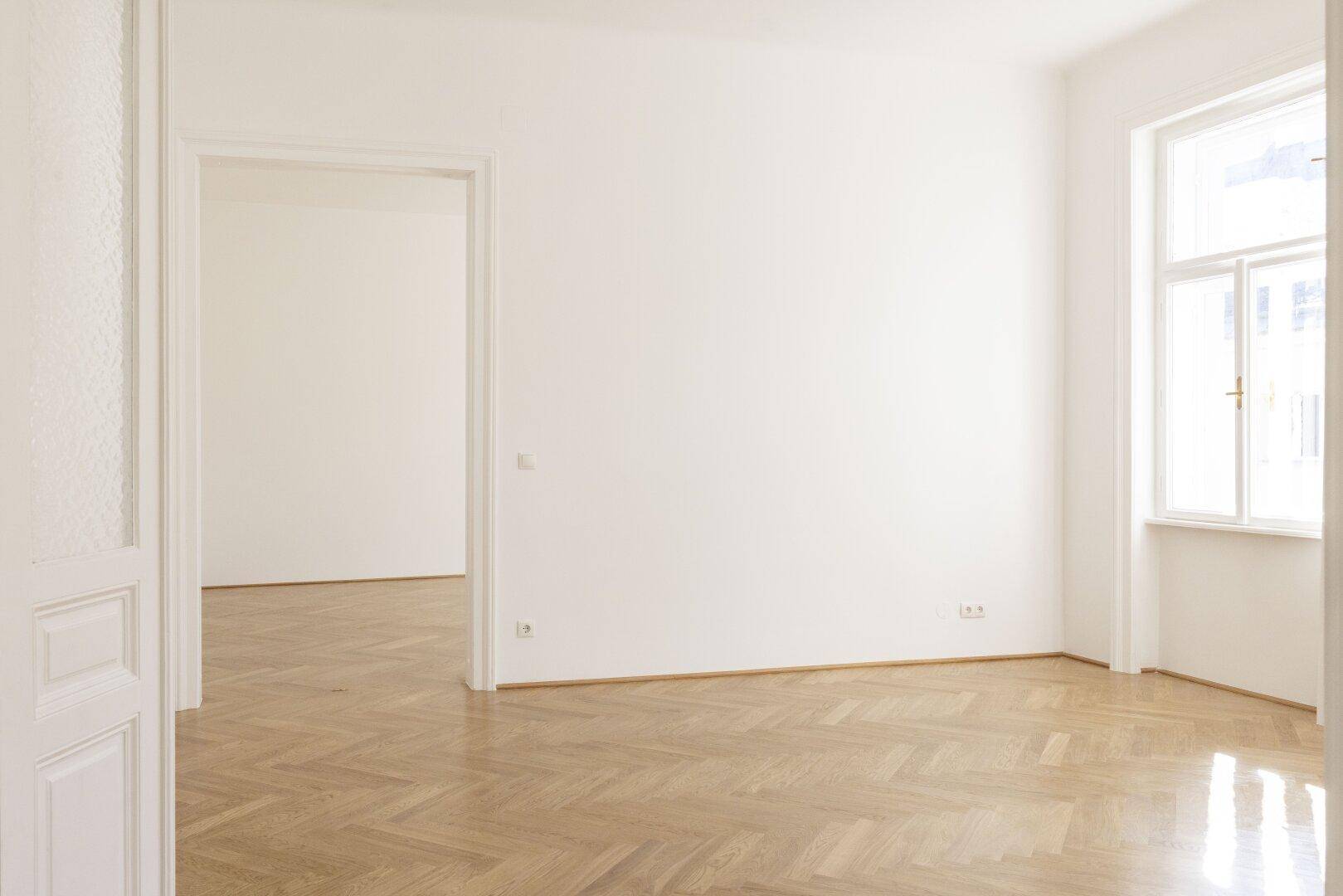 Geräumiger, leerer Raum mit Fischgrätparkettboden und weißen Wänden, bereit zur individuellen Gestaltung.