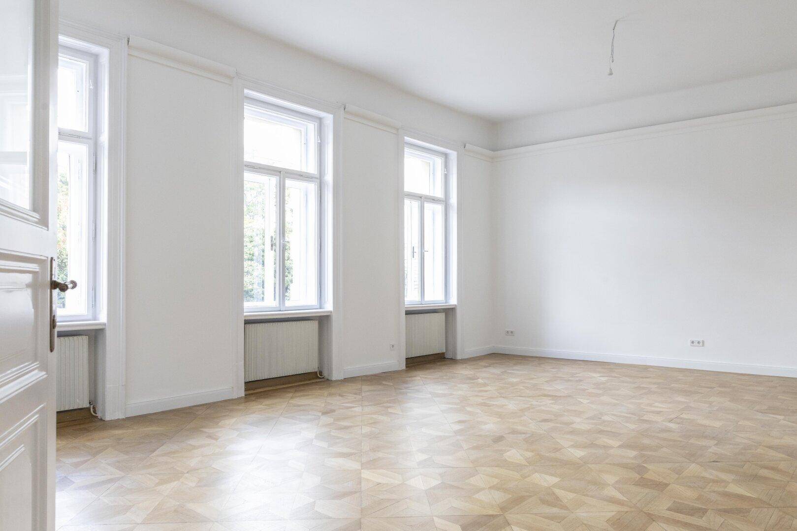 Geräumiger, heller Raum mit Parkettboden und zwei großen Fenstern, die viel Licht spenden.