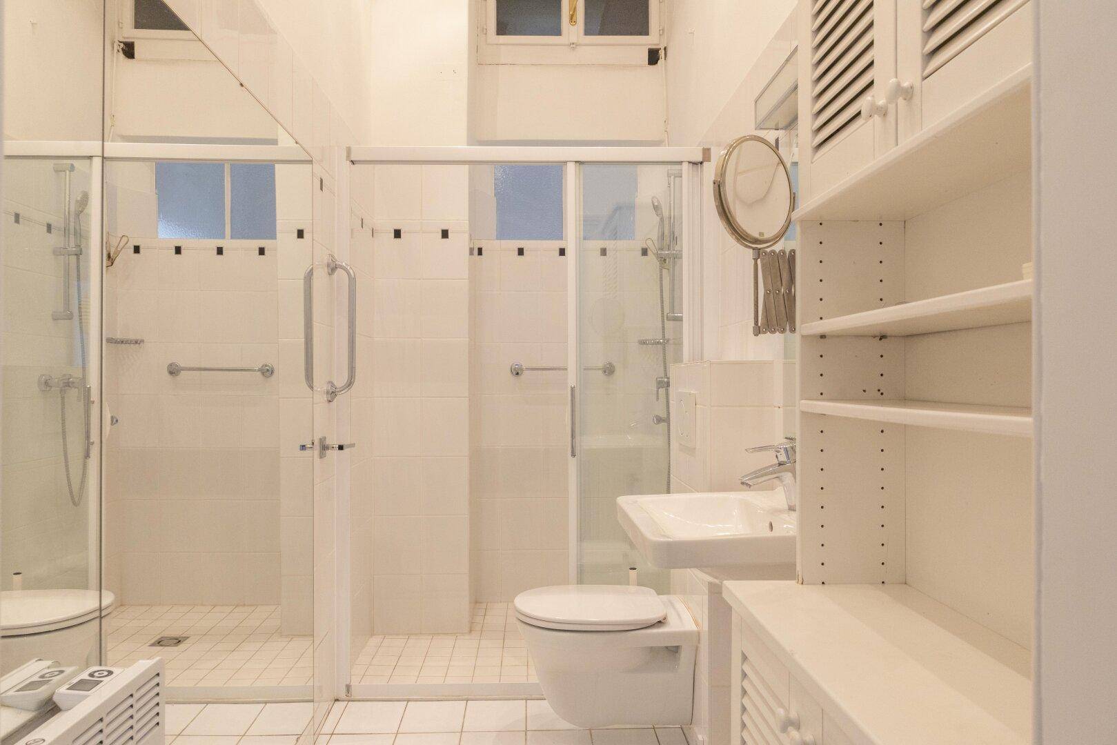 Modernes Badezimmer mit weiß gefliestem Boden, begehbarer Dusche, Toilette und Waschbecken.