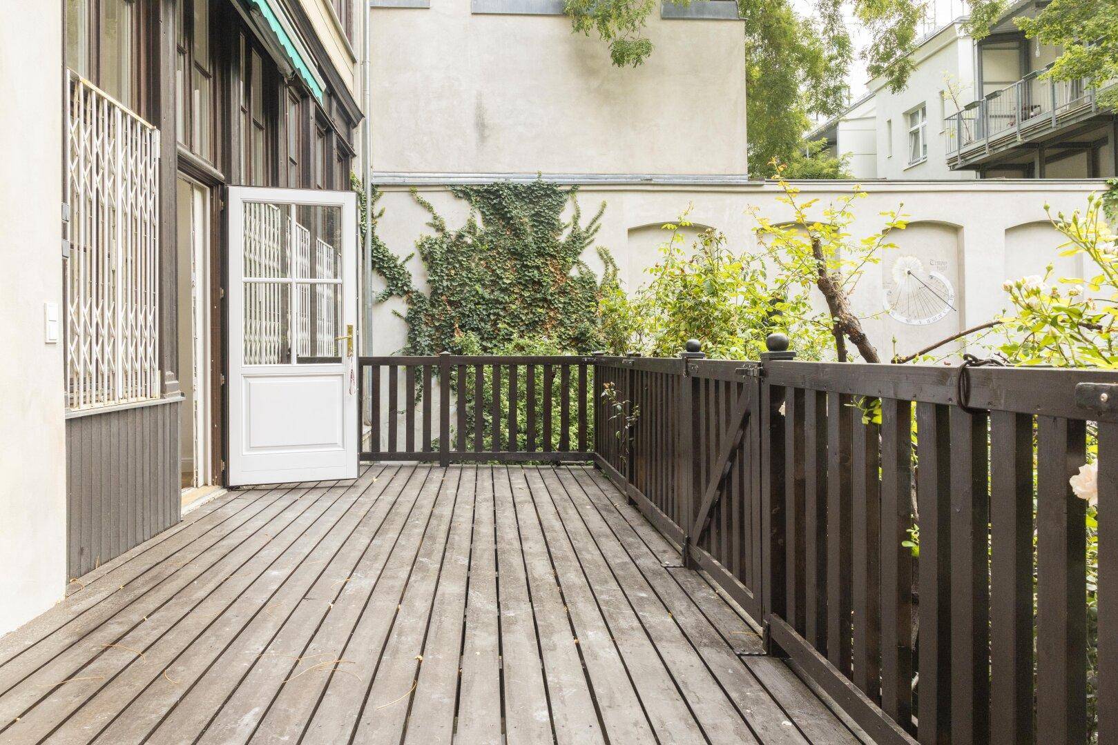 Breite Holzterrasse mit dunklem Geländer und Zugang zum grünen Gartenbereich, perfekt für Outdoor-Aktivitäten.