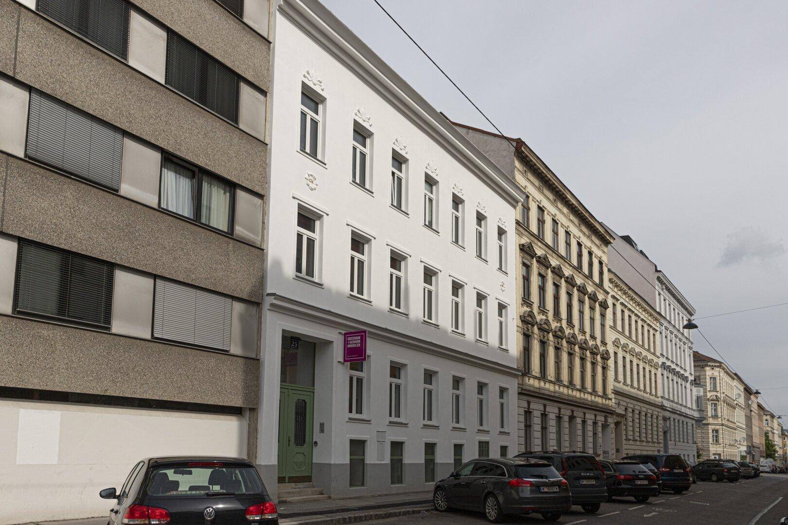Seitenansicht der renovierten Gebäudefassade in einer städtischen Umgebung mit parkenden Autos.
