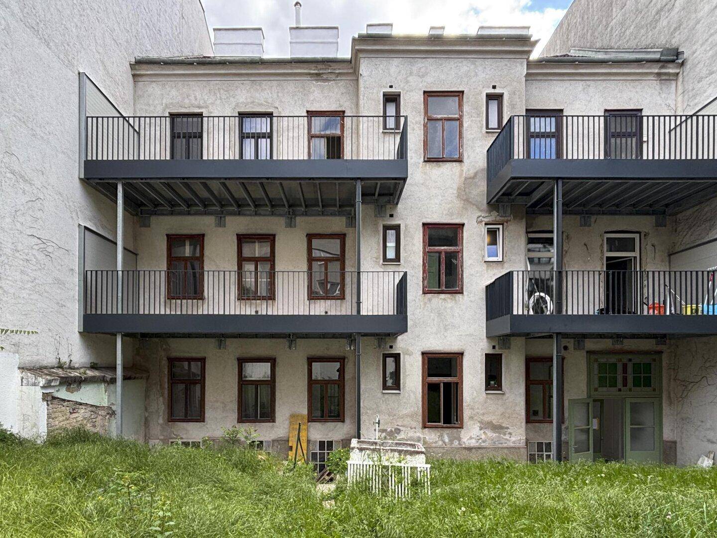 Rückansicht des Gebäudes mit Balkonen und einem naturbelassenen Gartenbereich im Innenhof.