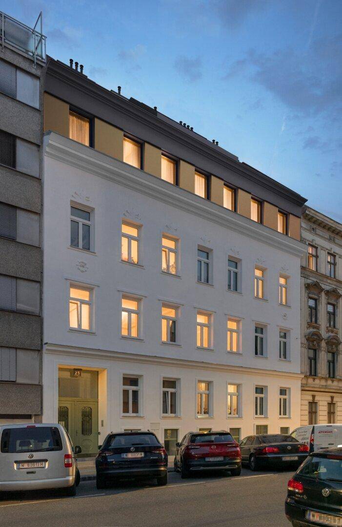 Renovierte Fassade eines Wohngebäudes bei Dämmerung mit beleuchteten Fenstern.
