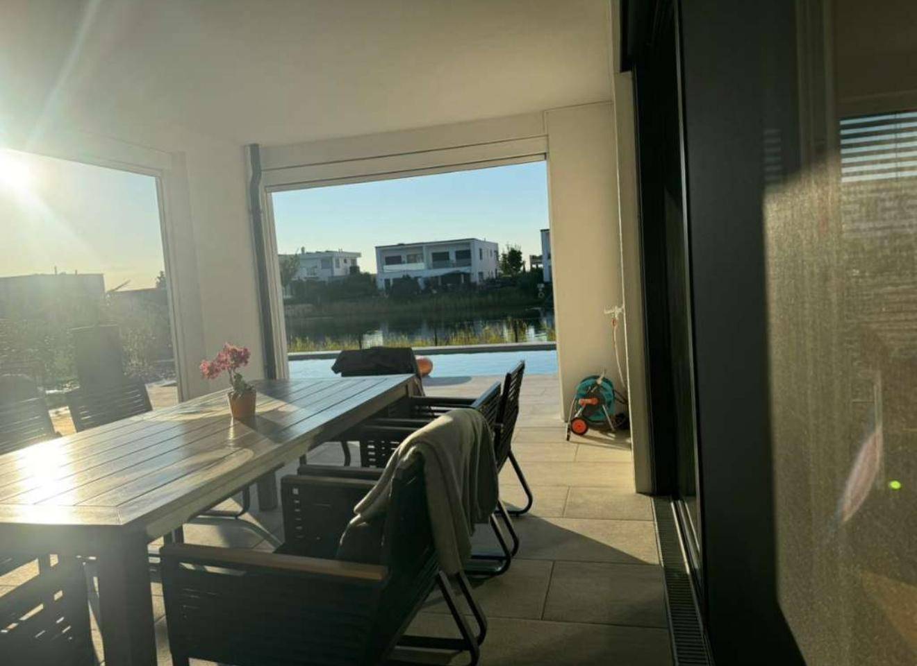Überdachte Terrasse mit Esstisch und Stühlen, bietet Blick auf den See.