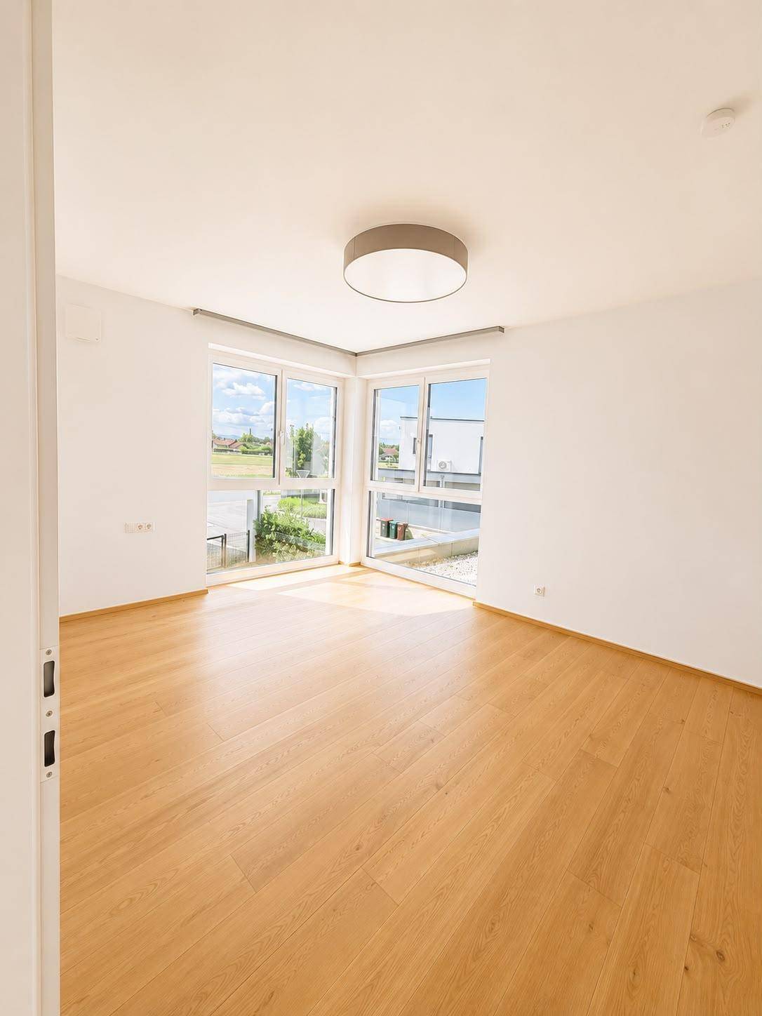 Helles Schlafzimmer mit Holzboden und großen Fenstern mit Blick ins Grüne.