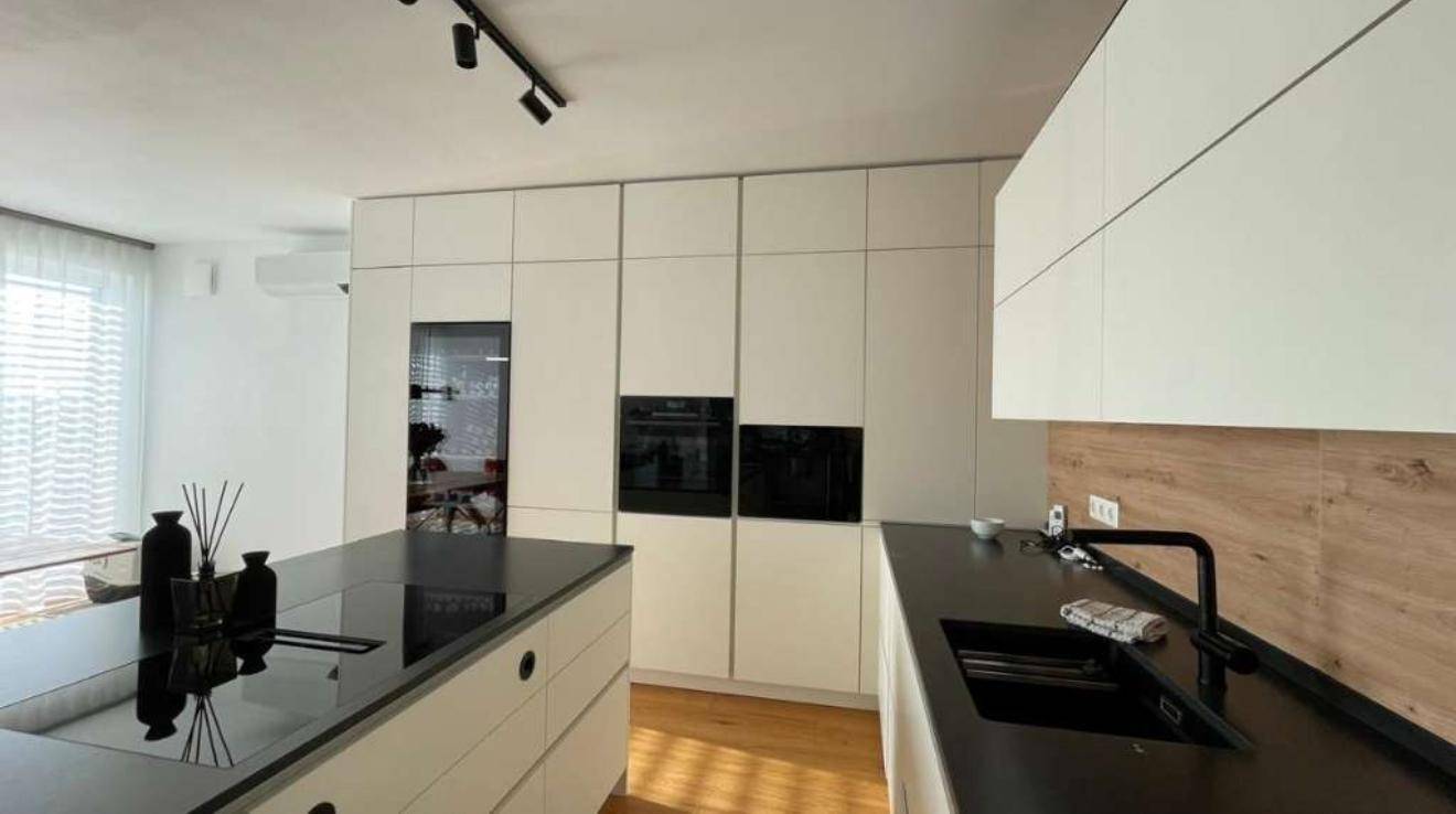 Moderne Küche mit weißen Schränken, schwarzer Arbeitsplatte und integrierten Geräten.