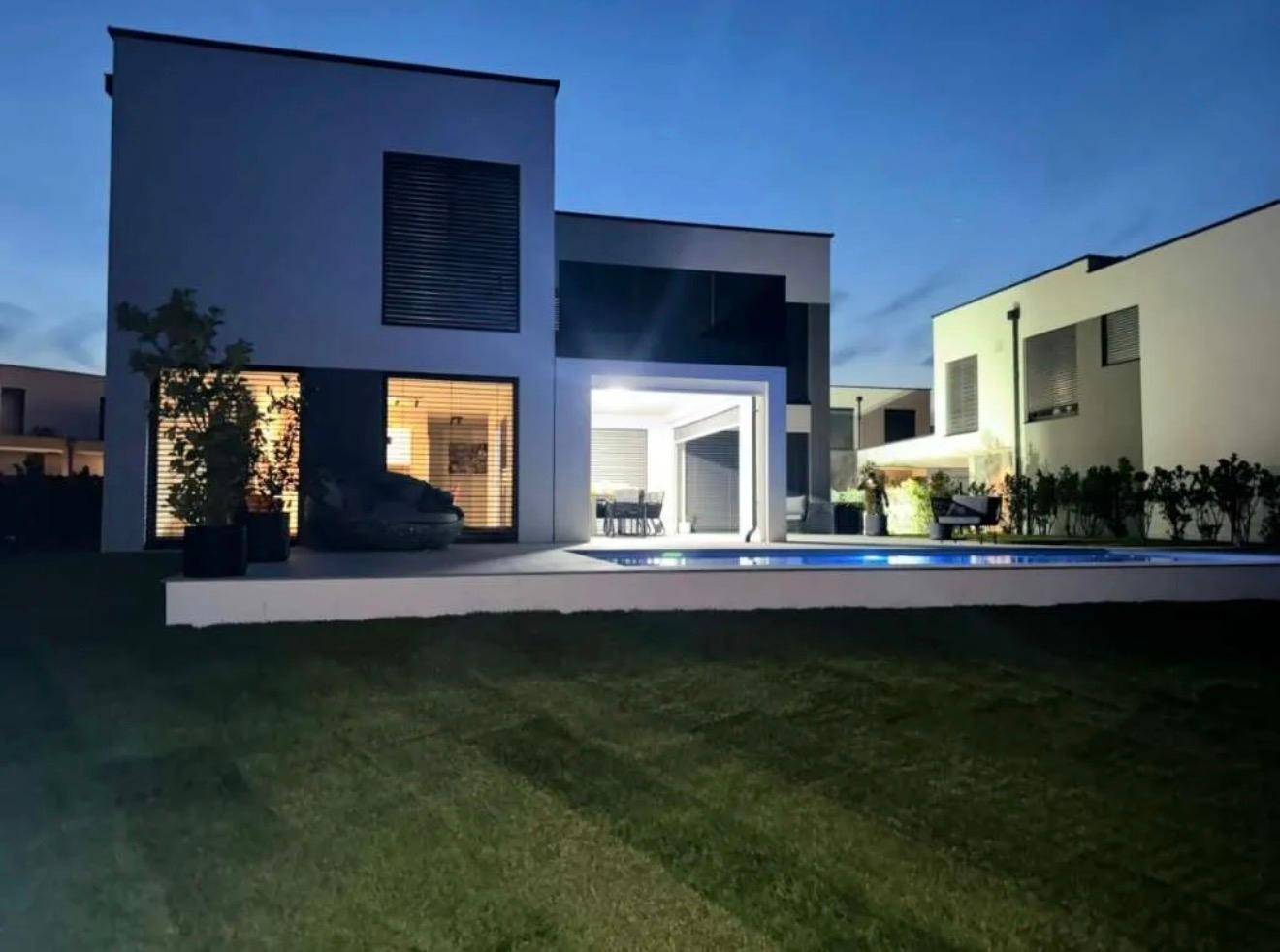 Moderne Villa bei Nacht mit beleuchtetem Pool und Garten.