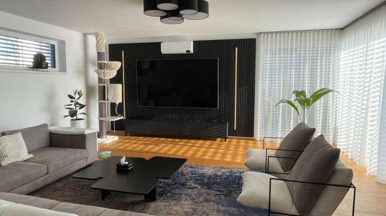 Modernes Wohnzimmer mit Holzboden, großem Fernseher und viel Tageslicht.