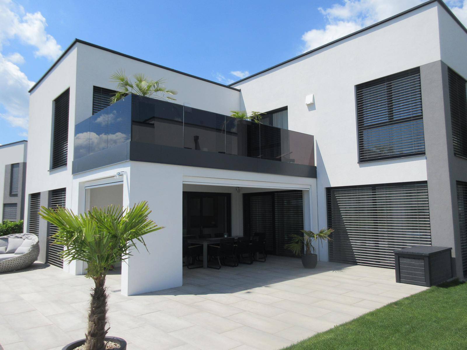 Moderne Villa mit überdachter Terrasse und Balkon mit Glasgeländer.