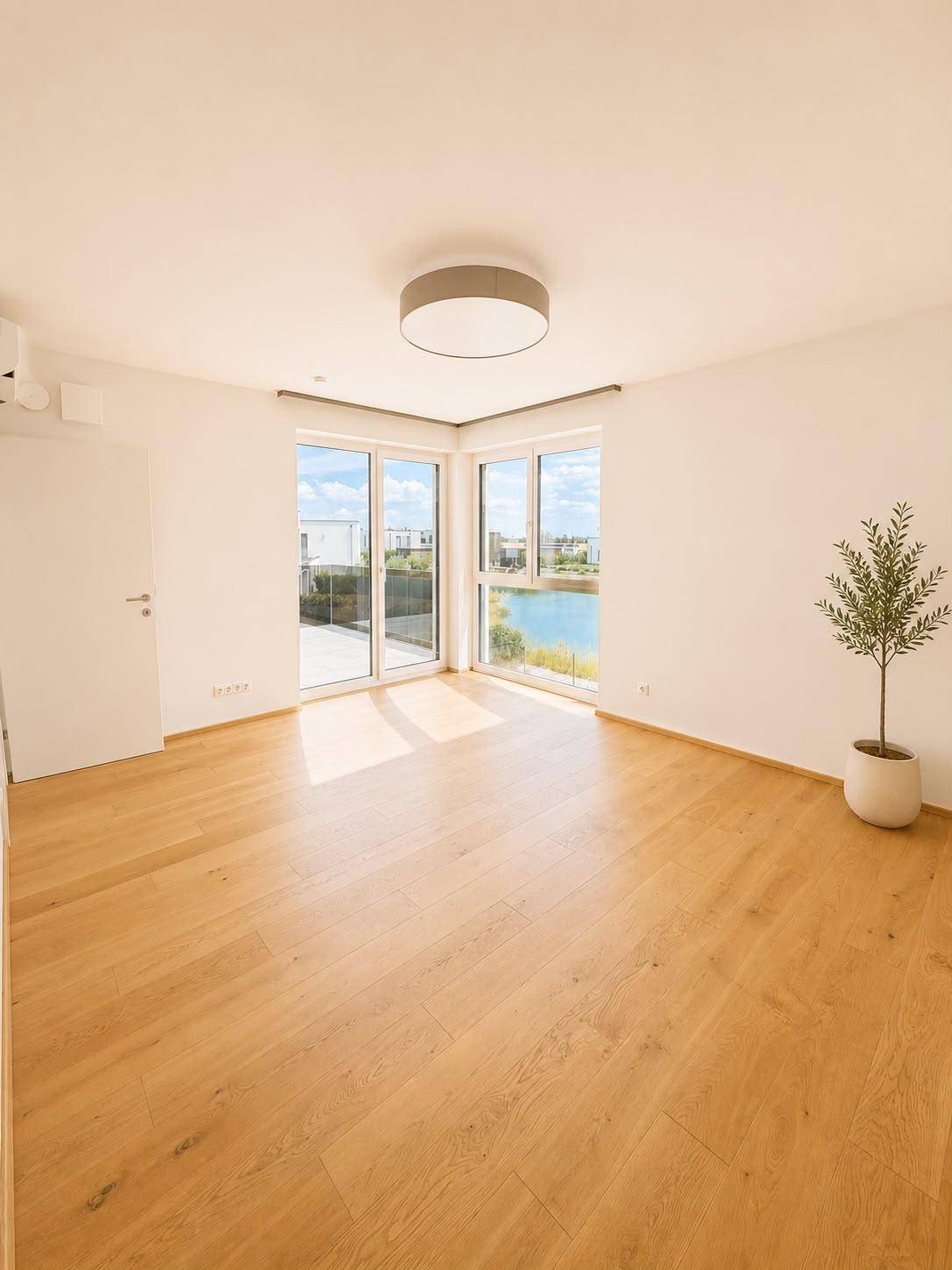 Geräumiges Schlafzimmer mit Holzboden, großen Fenstern und Seeblick.