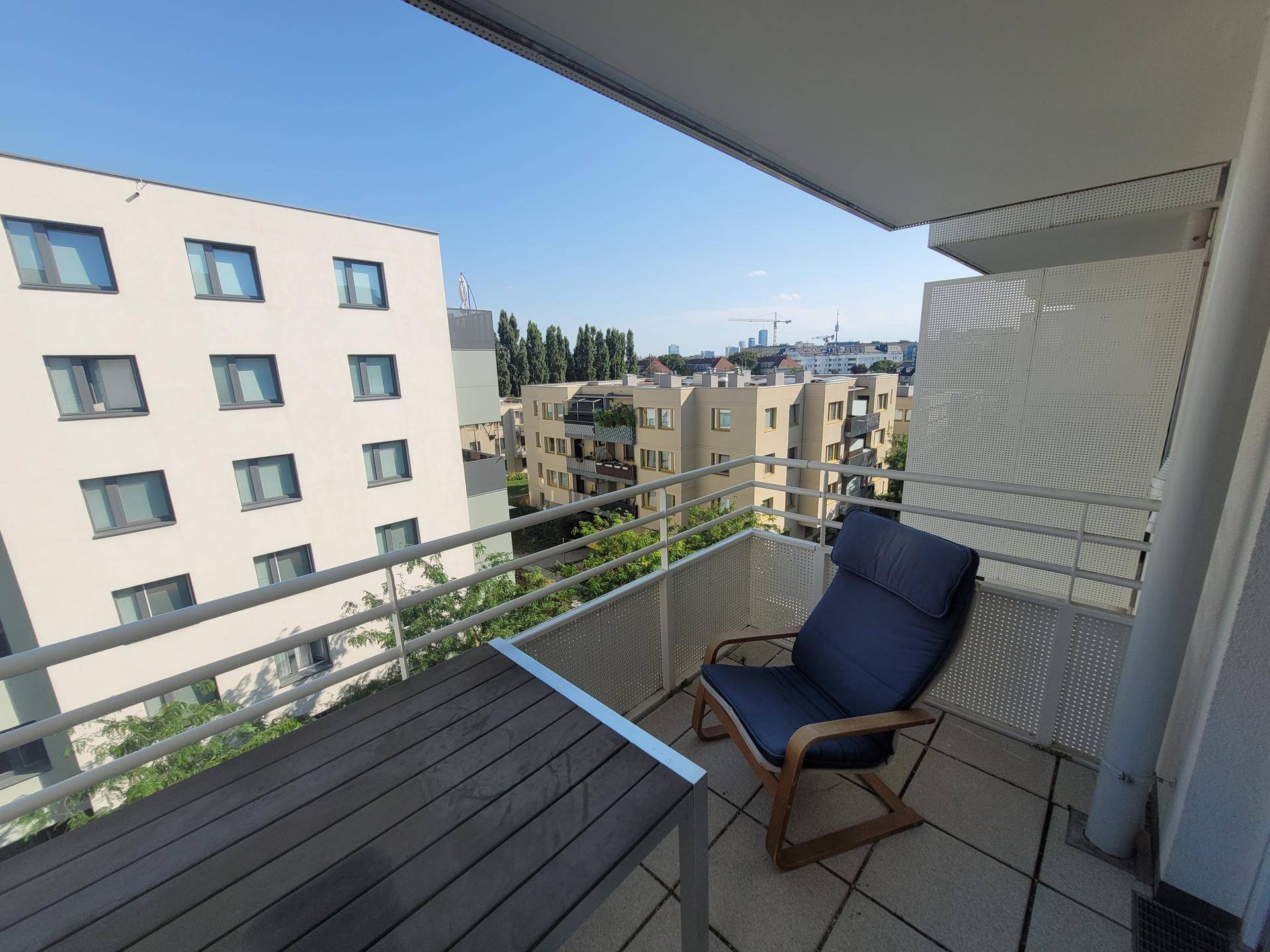 Sonniger Balkon mit Sitzgelegenheiten und Blick auf die umliegenden Gebäude und die Stadt.