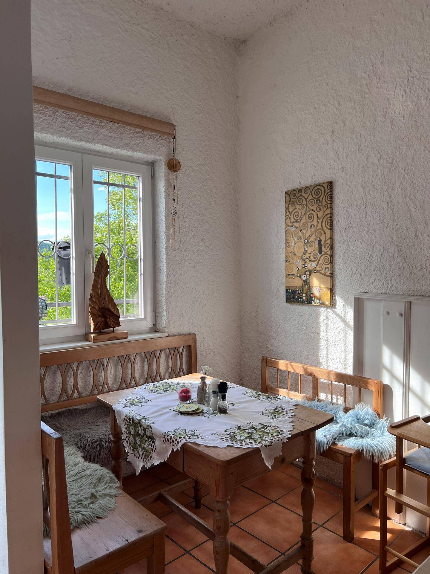 Eine gemütliche Essecke mit Holztisch und Bänken, Terrakottafliesen und einem Fenster mit Blick ins Grüne.