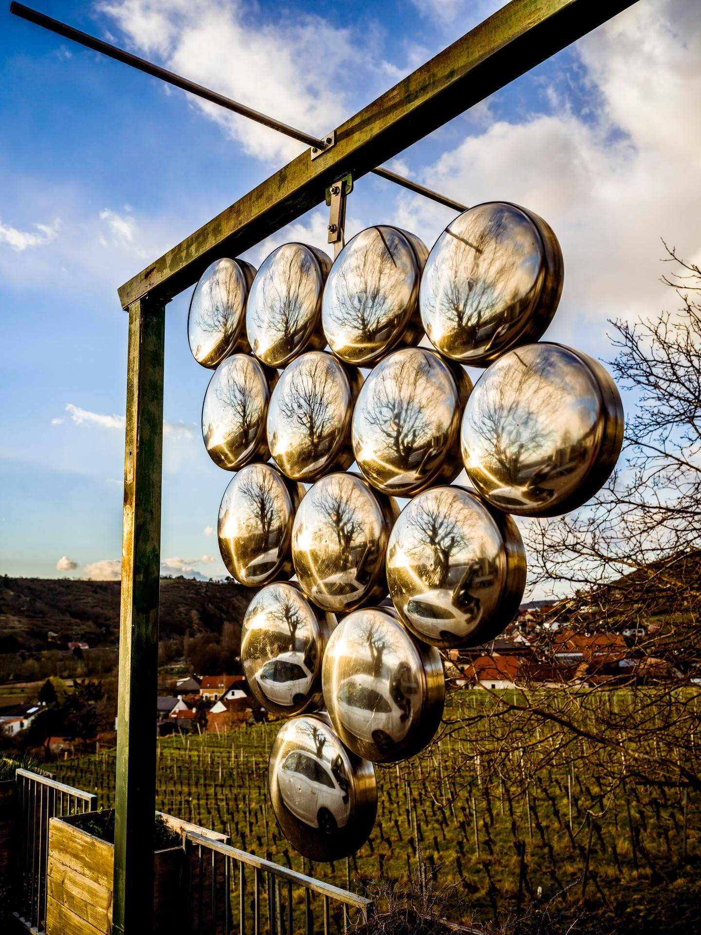 Eine Kunstinstallation in Form einer Weintraube aus reflektierenden Kugeln mit Weinbergen im Hintergrund.