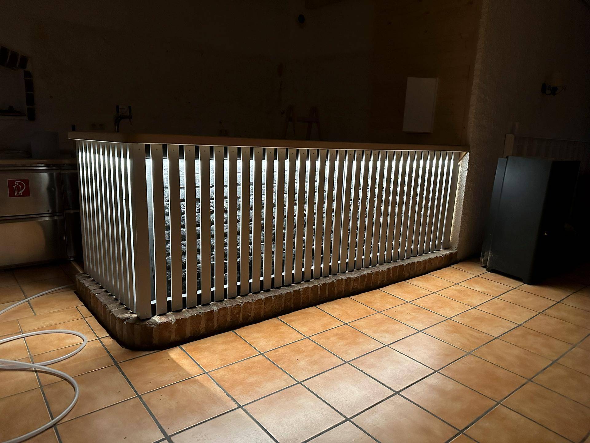 Ein schwach beleuchteter Raum mit Terrakottafliesen und einer beleuchteten Holzkonstruktion, möglicherweise eine Bar.