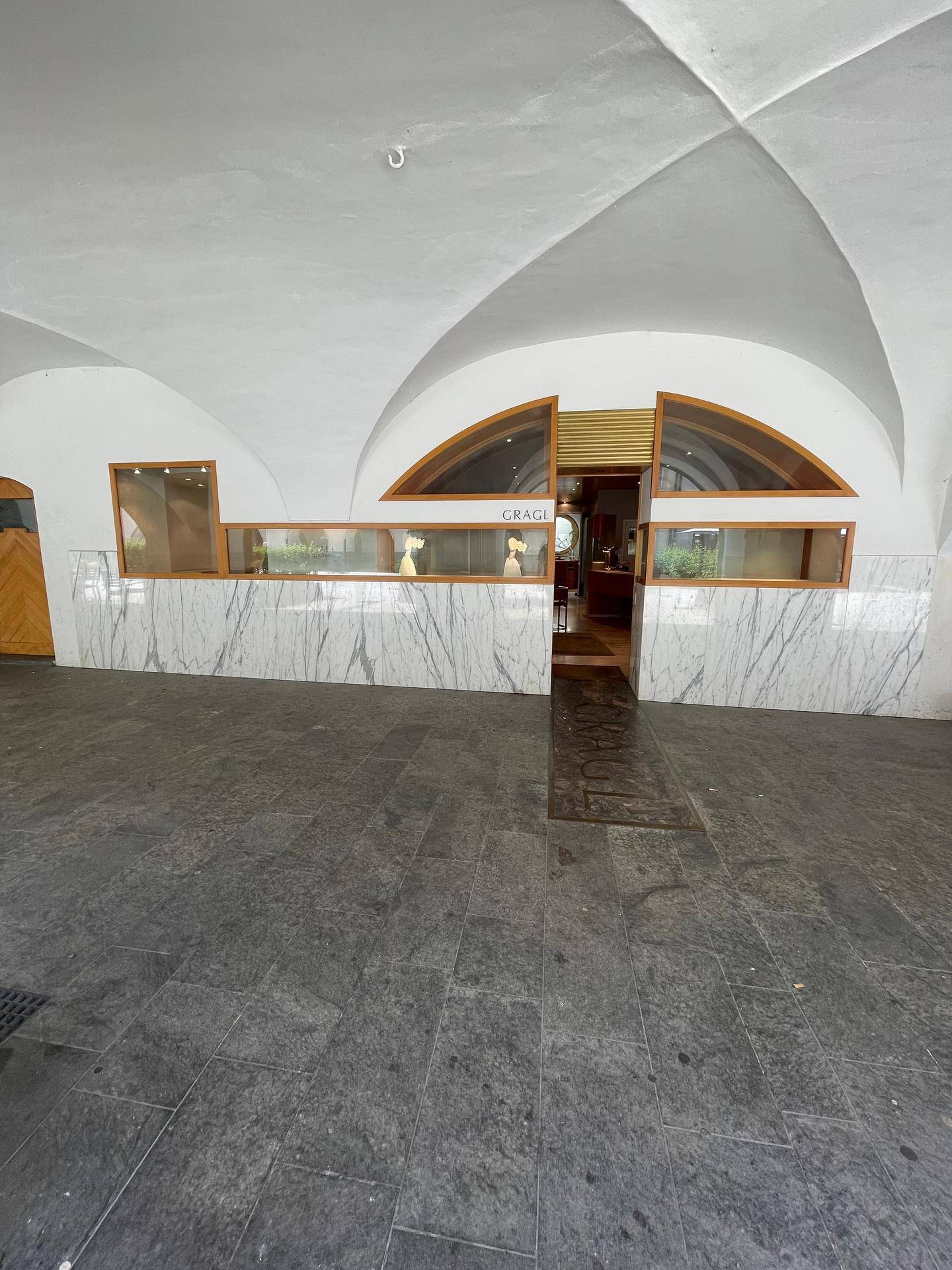 Eingangsbereich eines Geschäfts unter einem Gewölbe mit Marmorverkleidung und Schaufenstern.